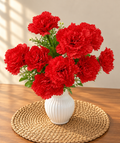 Artificial red carnation bouquet in white ribbed vase on woven mat